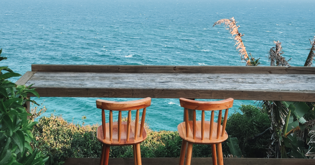 2 wooden stools in front of a cliff side ocean view