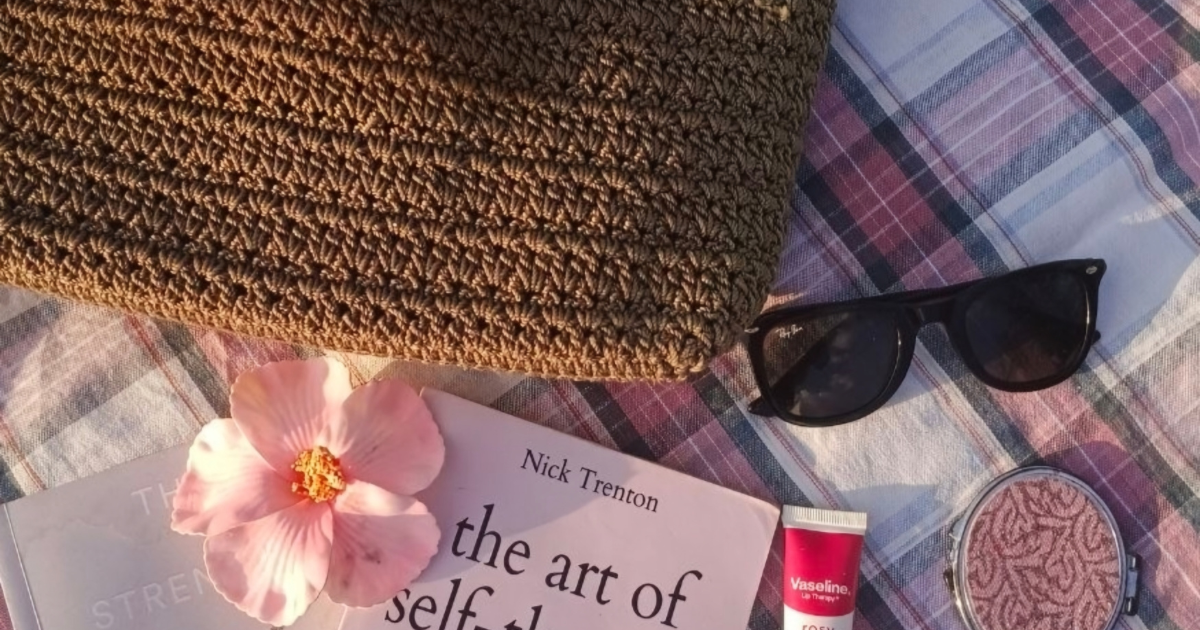 sunglasses, a woven tote and a book with a pink flower in the style of a flat lay